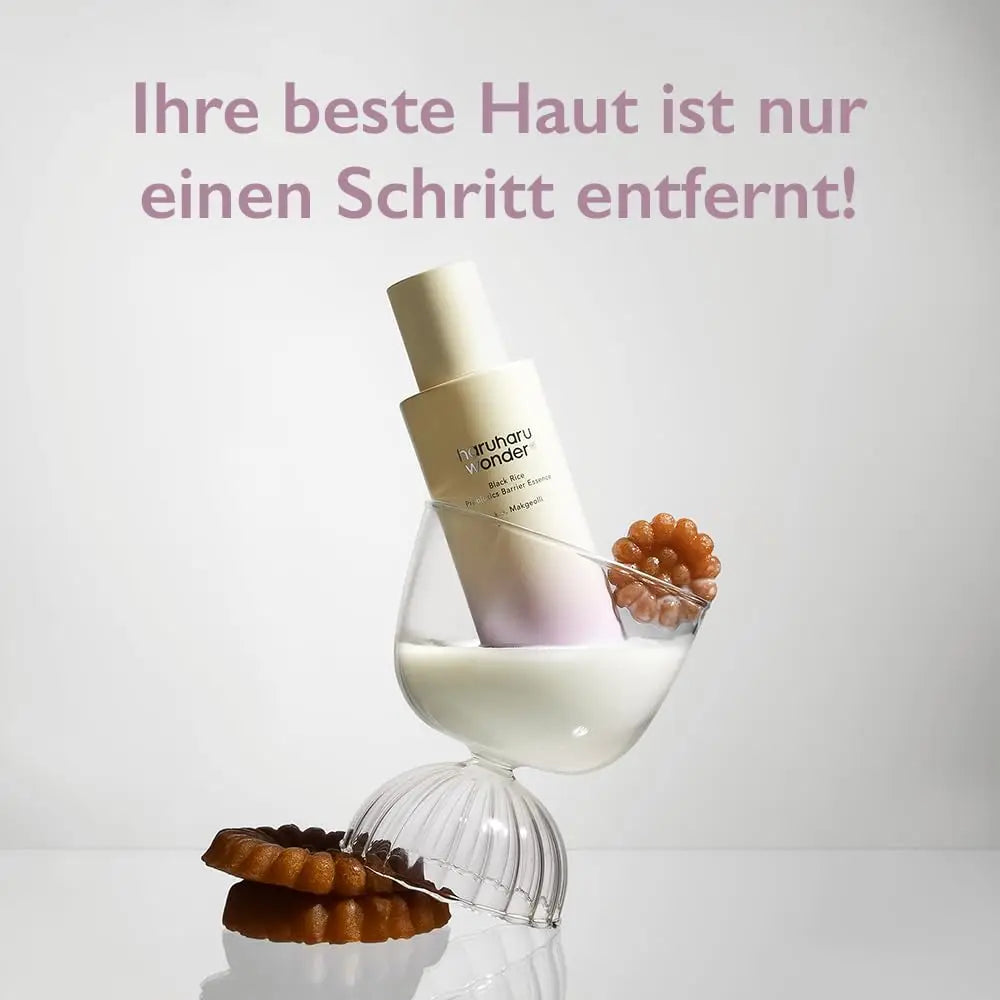 haruharu wonder Black Rice Probiotics Barrier Essence 120ml bottle tilted inside a glass filled with milk, accompanied by two brown flower-shaped cookies on a white background with German text above.