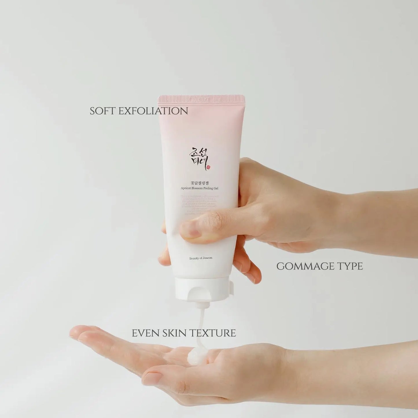 A hand dispensing a white gel from a pink and white tube of Beauty of Joseon Apricot Blossom Peeling Gel 100ml, promoting soft exfoliation and even skin texture.