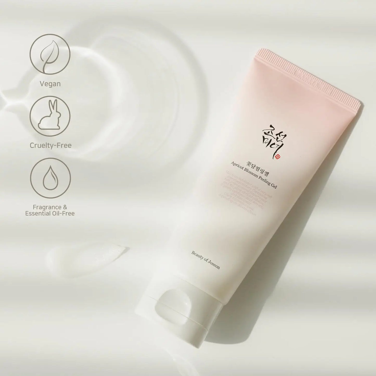 Beauty of Joseon Apricot Blossom Peeling Gel 100ml tube with soft pink gradient packaging lying on a white surface, highlighting vegan, cruelty-free, and fragrance-free features.
