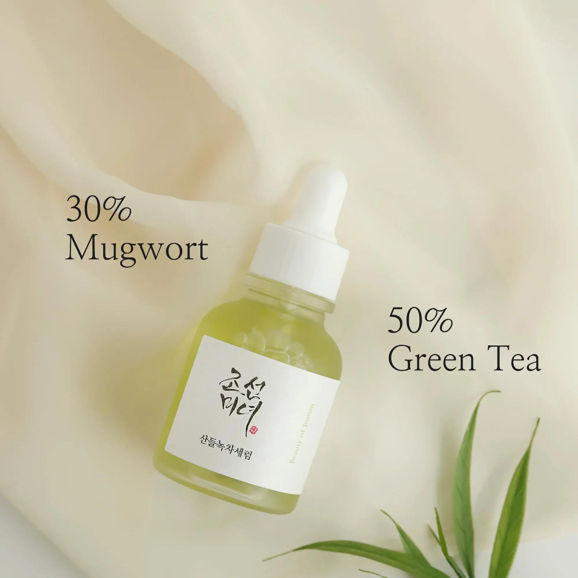 Beauty of Joseon Calming Serum Green Tea Panthenol 30ml in a glass dropper bottle highlighting 50% green tea and 30% mugwort ingredients on a soft cream-colored fabric background with green leaves.