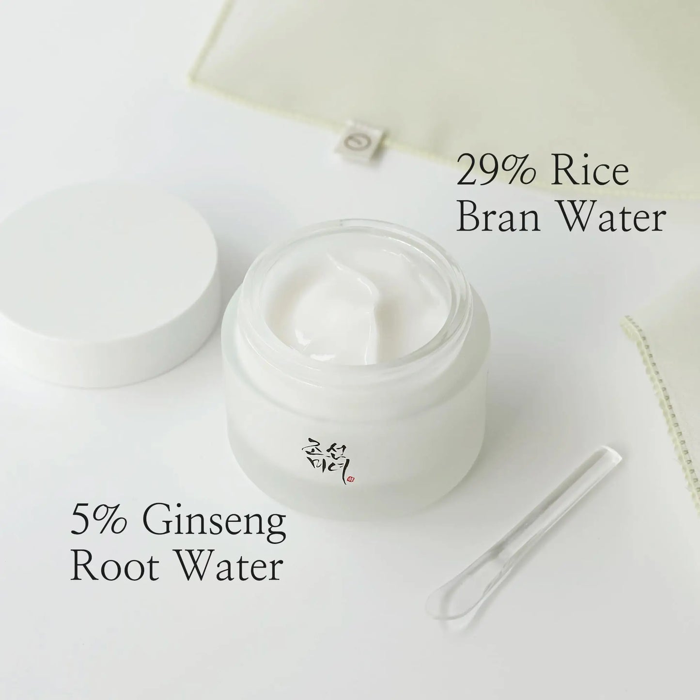 Open jar of Beauty of Joseon Dynasty Cream 100ml showing white cream inside, accompanied by a small clear spatula and text highlighting 29% rice bran water and 5% ginseng root water ingredients.