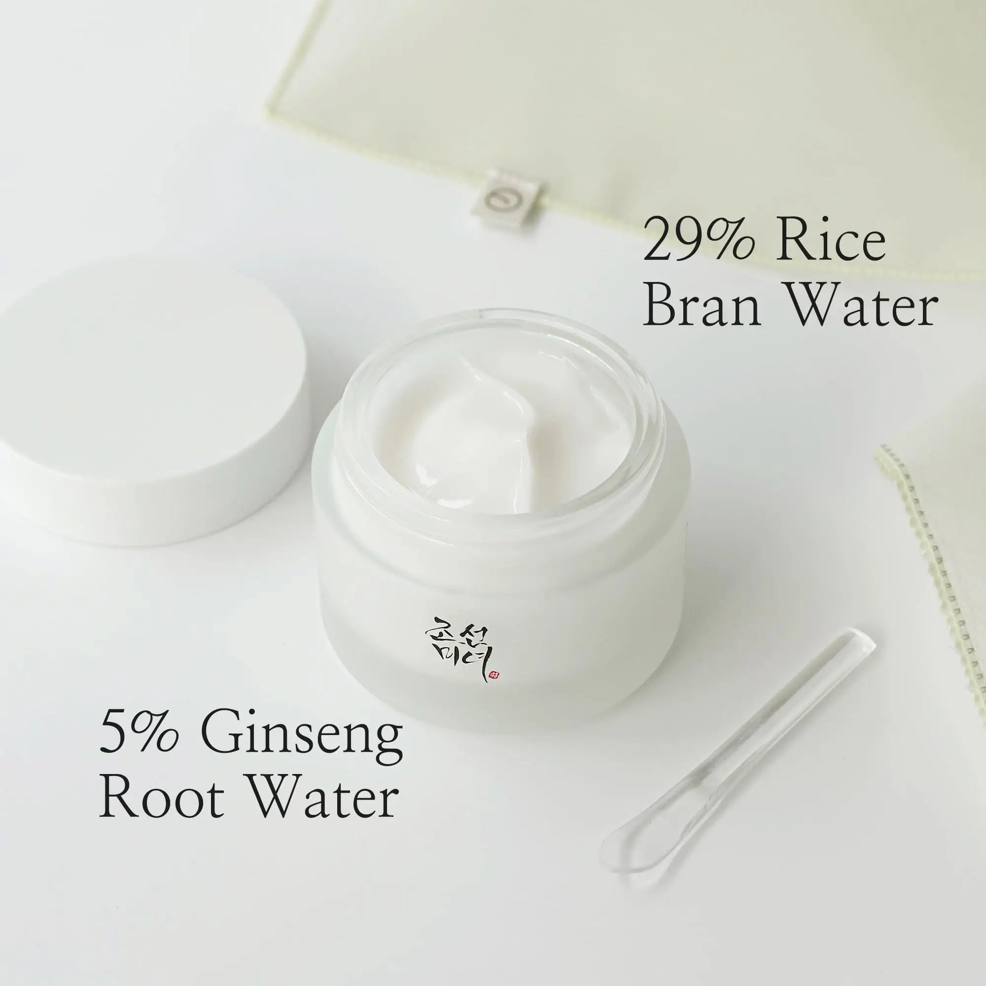 Open jar of Beauty of Joseon Dynasty Cream 100ml showing white cream inside, accompanied by a small clear spatula and text highlighting 29% rice bran water and 5% ginseng root water ingredients.