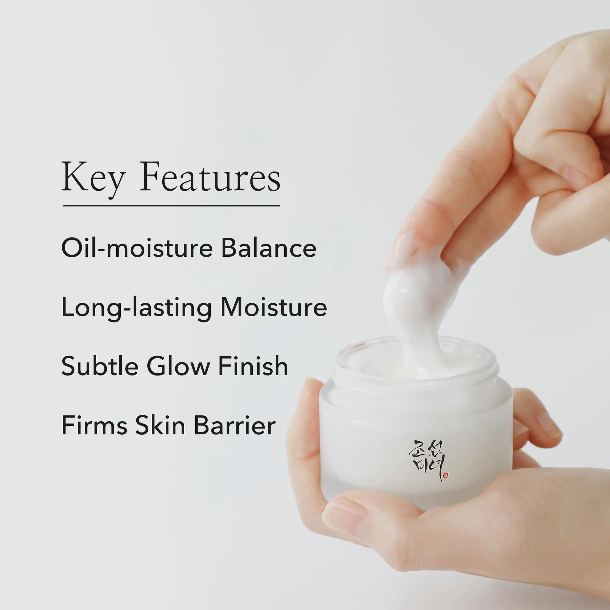 Hand holding an open jar of Beauty of Joseon Dynasty Cream 100ml with a finger scooping out cream, alongside text listing key features: oil-moisture balance, long-lasting moisture, subtle glow finish, firms skin barrier.
