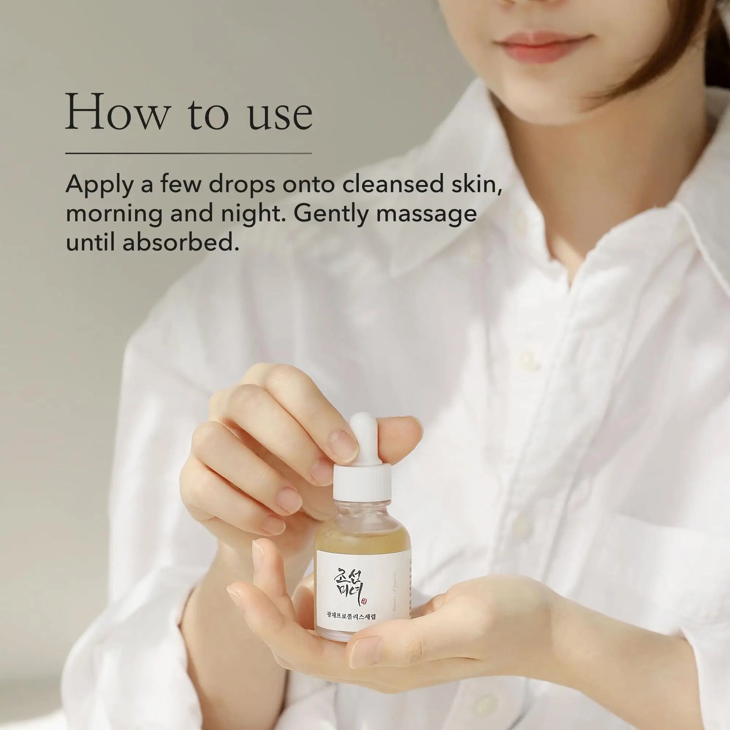 Woman holding a bottle of Beauty of Joseon Glow Serum Propolis and Niacinamide 30ml with instructions to apply a few drops onto cleansed skin morning and night and gently massage until absorbed.