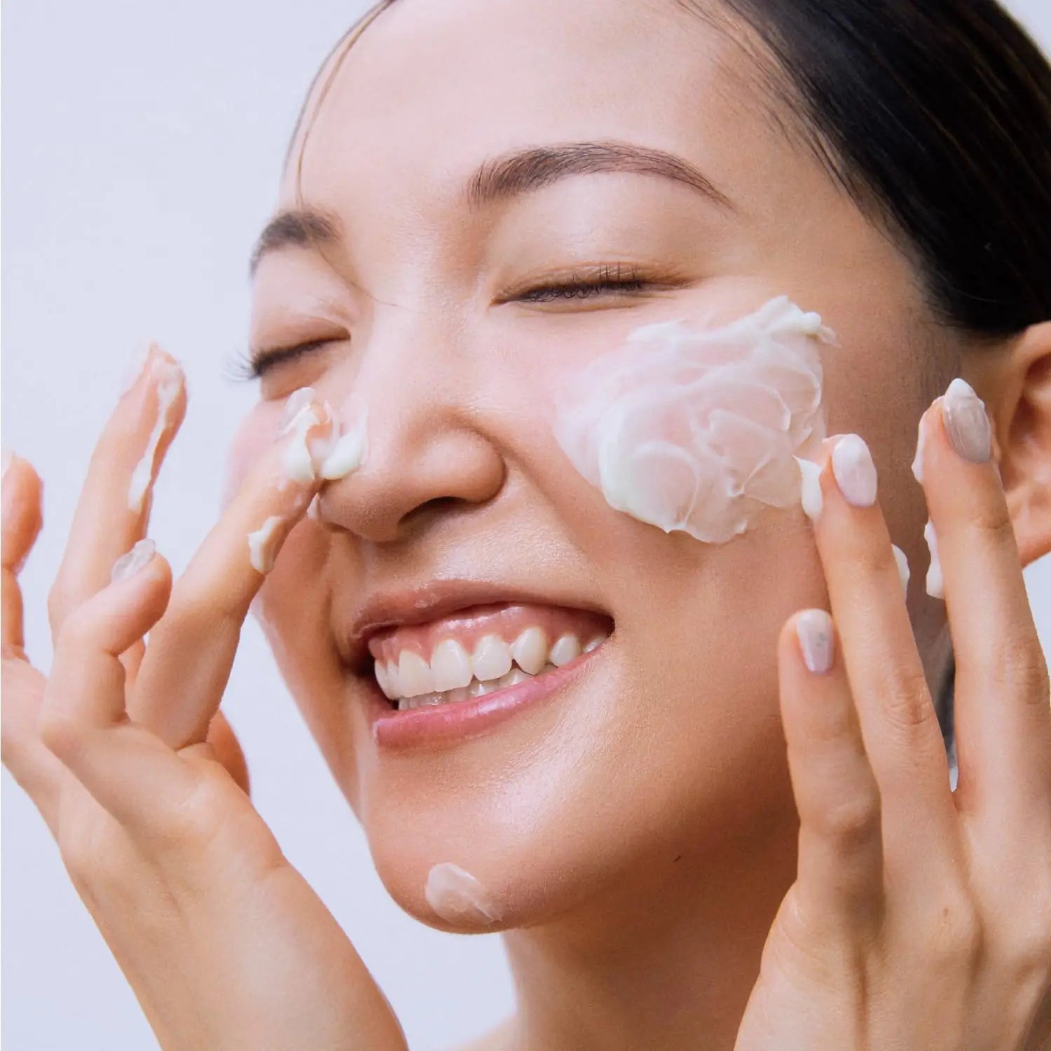 Smiling woman gently applying Beauty of Joseon Jelloskin Massage Cream for Face and Body 200ml on her cheeks with fingers for smooth, hydrated skin.