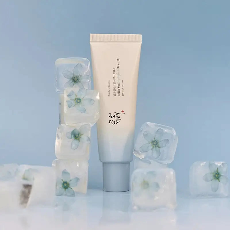 Tube of Beauty of Joseon Relief Sun Aqua-Fresh : Rice + B5 sunscreen standing among clear ice cubes with embedded delicate flowers on a pale blue background.