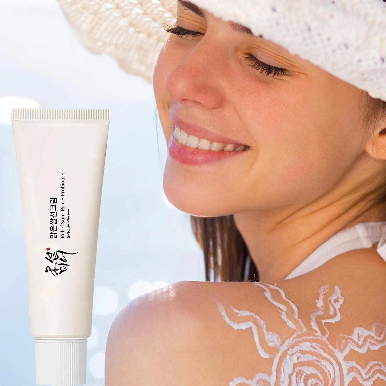 Smiling woman wearing a white sunhat applies sunscreen with a sun-shaped design on her shoulder alongside a tube of Beauty of Joseon Relief Sun : Rice + Probiotics 50ml.