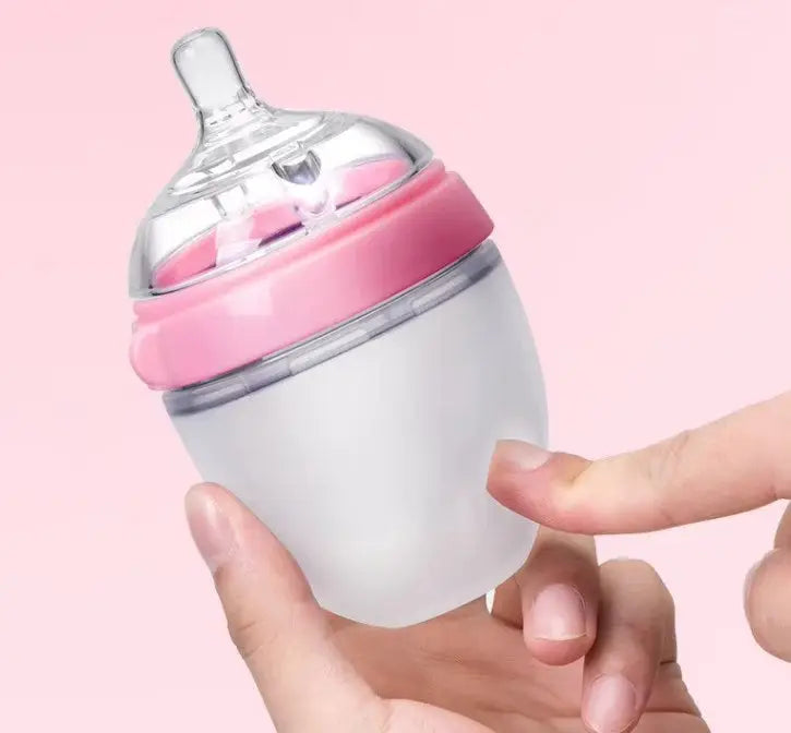 Hand holding a small silicone baby bottle with a pink ring and clear adjustable flow teat against a soft pink background, showcasing BPA Free Anti Colic Silicone Breastfeeding Bottle. 150 ml Bottle with Adjustable Flow Teat + 250 ml Bottle with Adjustable Flow Teat for Baby Milk and Breastfee.