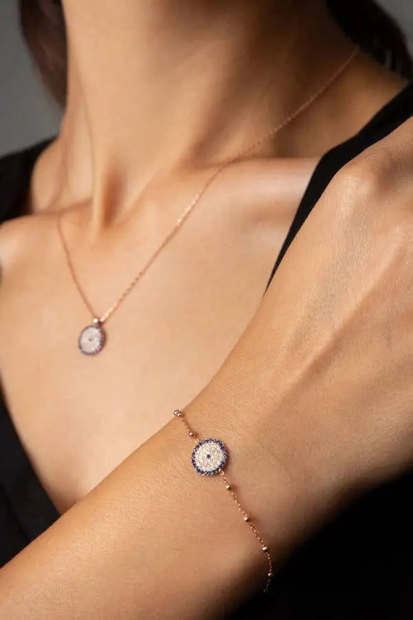 Close-up of a woman wearing an Einzelstück - 14K Gold Plated Nazar Rose Gold Bracelet with blue zircona crystals - Rose Gold Bracelet- Gold Bracelet Gift for Women on her wrist paired with a matching necklace.