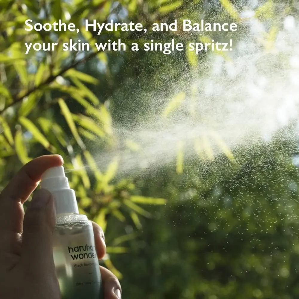 Hand holding and spraying haruharu wonder Black Bamboo Mist 150ml with a fine mist against a blurred green bamboo background and sunlight filtering through leaves.