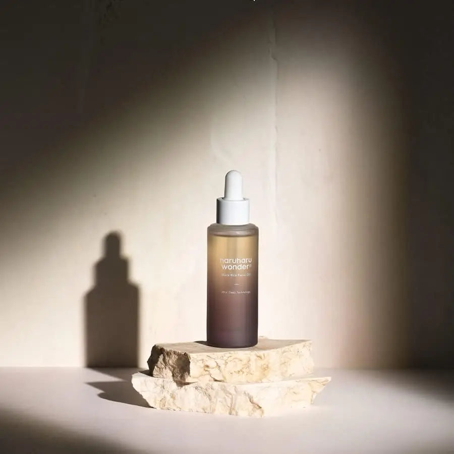 haruharu wonder Black Rice Facial Oil 30ml bottle with dropper on stacked natural stone against a neutral background with soft lighting and shadow effects