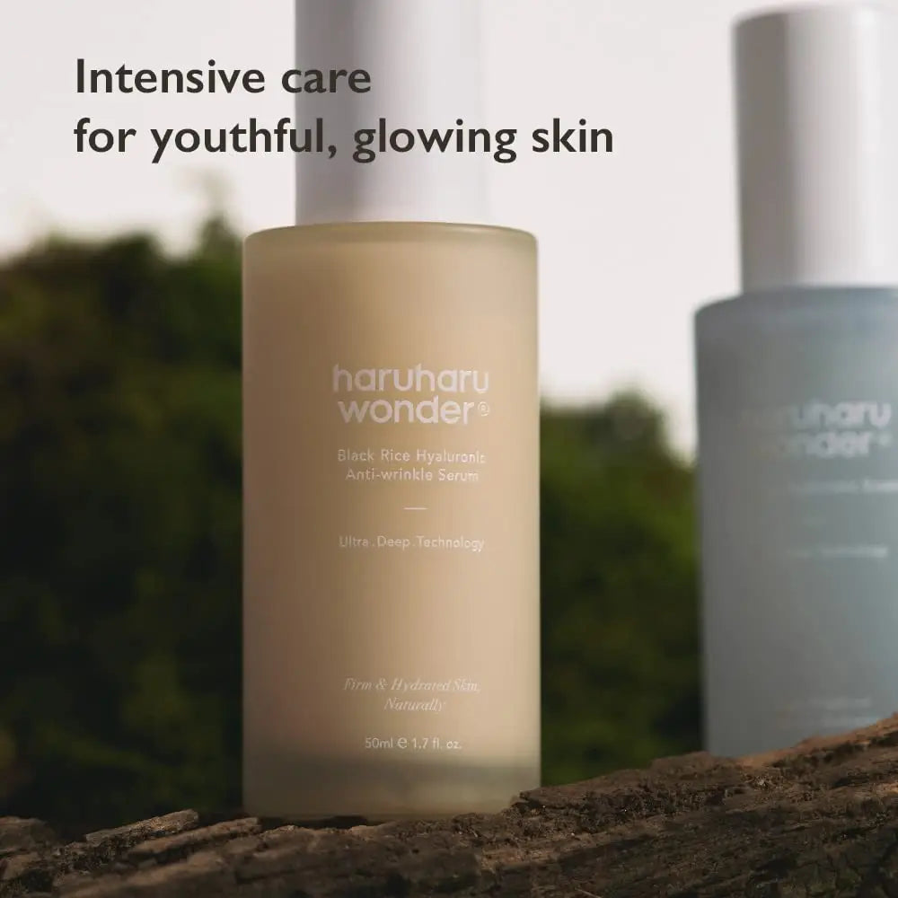 Close-up of a frosted glass bottle labeled haruharu wonder Black Rice Hyaluronic Anti-Wrinkle Serum 50 ml placed on natural wooden surface with blurred background and text saying Intensive care for youthful, glowing skin.