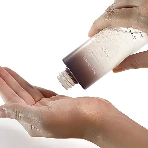 Person pouring haruharu wonder Black Rice Hyaluronic Toner for Sensitive Skin 150ml into palm, showcasing clear liquid texture and elegant frosted bottle design.