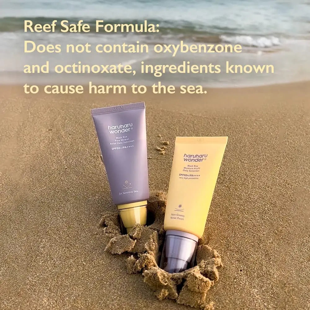 Two tubes of haruharu wonder Black Rice Moisture Airyfit Sunscreen 50ml partially buried in sand on a beach, with text highlighting its reef-safe formula free from oxybenzone and octinoxate.