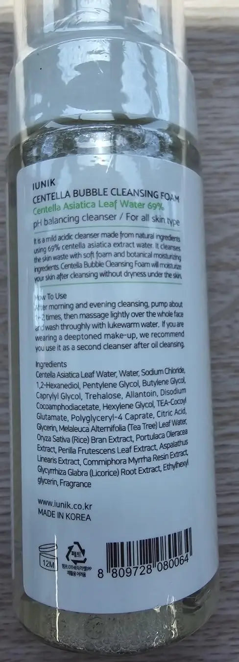 Clear bottle of iUNIK Centella Calming Daily Sunscreen 60ml + iUNIK Centella Bubble Cleansing Foam, 150ml showing product label with green and black text describing natural ingredients and usage instructions against a wood surface background.