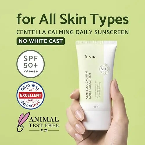 Hand holding a tube of iUNIK Centella Calming Daily Sunscreen 60ml with SPF 50+ PA++++ on a light green background, labeled for all skin types, no white cast, dermatologically tested, and animal test-free by PETA.