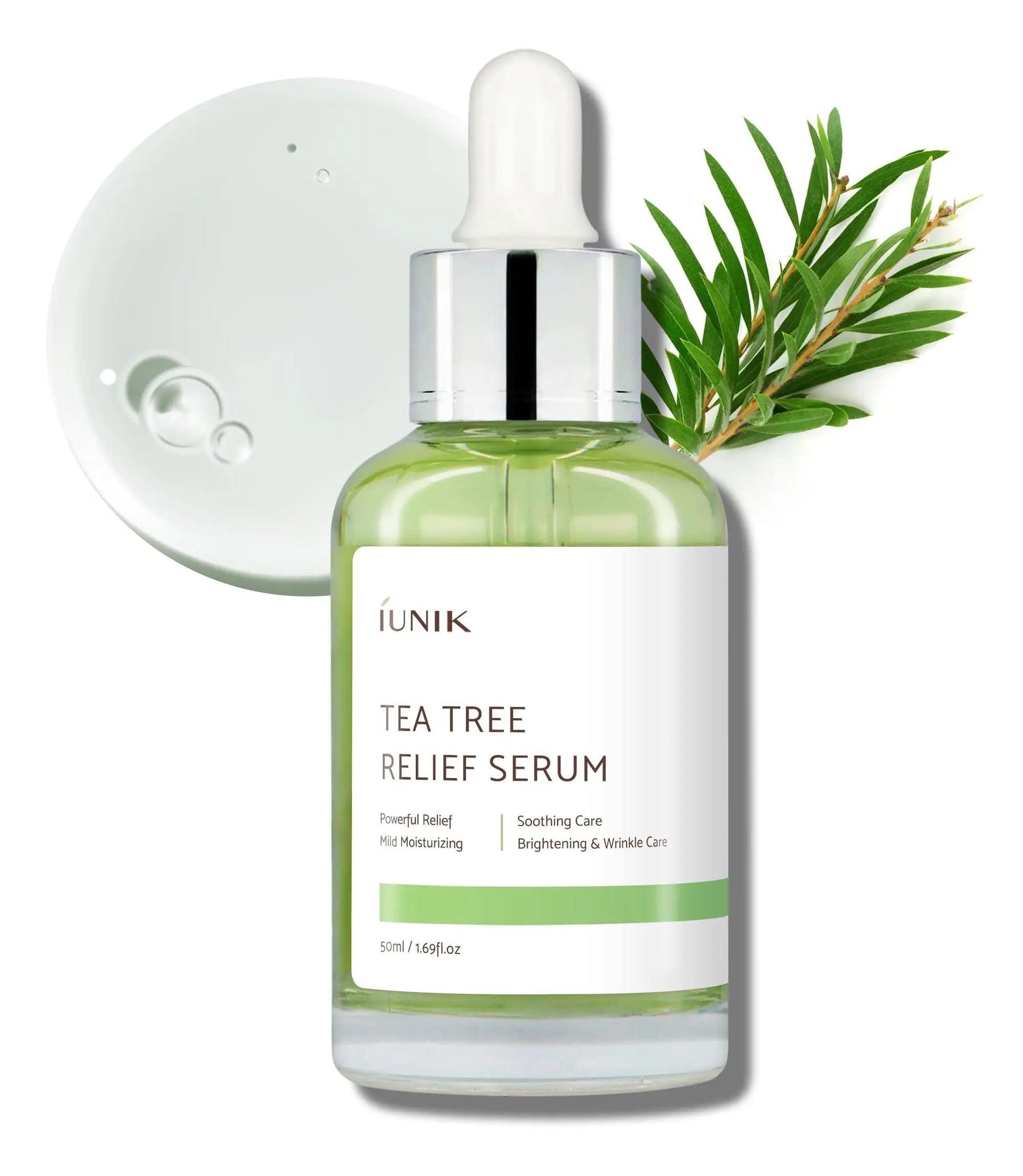 Clear glass dropper bottle of iUNIK Tea tree Relief Serum 50ml with green liquid, placed next to tea tree leaves and serum droplets on white background for soothing skincare.