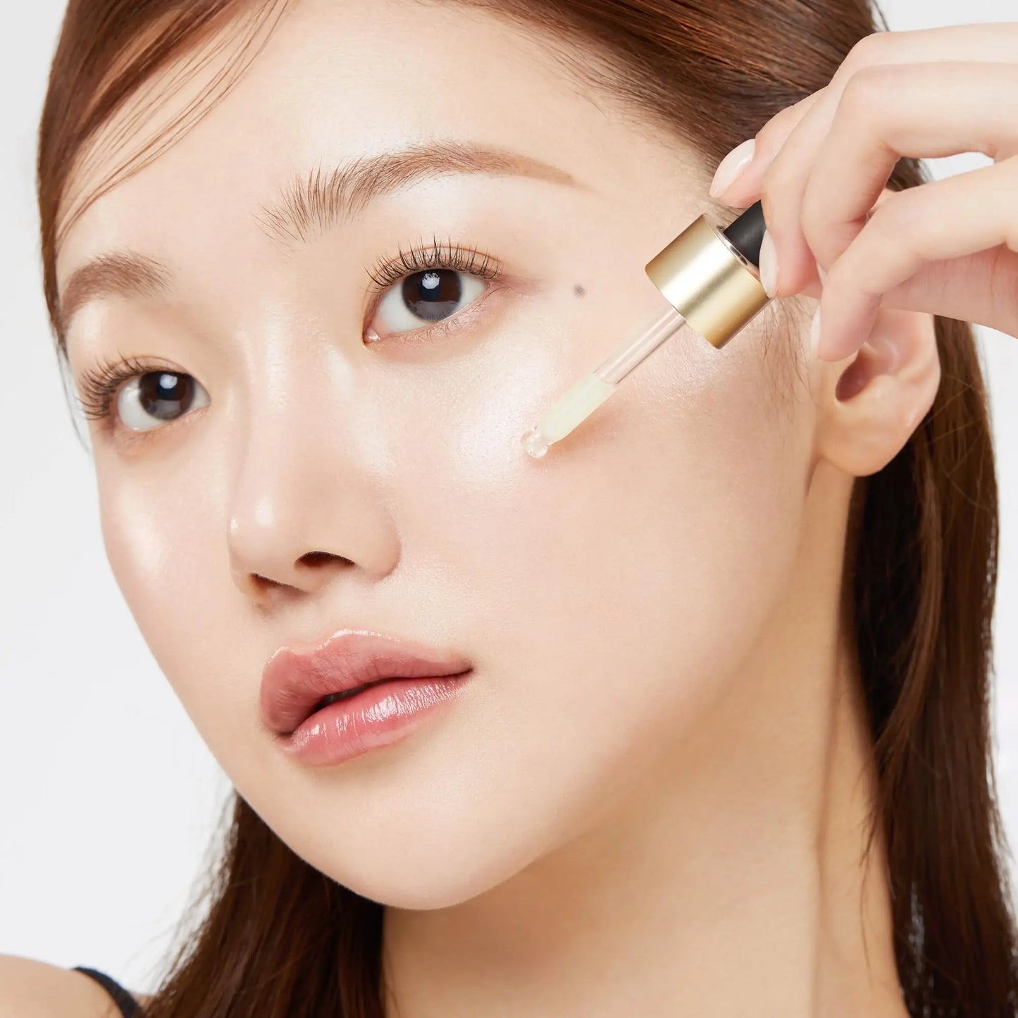 Close-up of a woman applying medicube AGE-R VITA C PRO AMPOULE 20ml serum with a dropper onto her cheek, showcasing smooth, glowing skin.