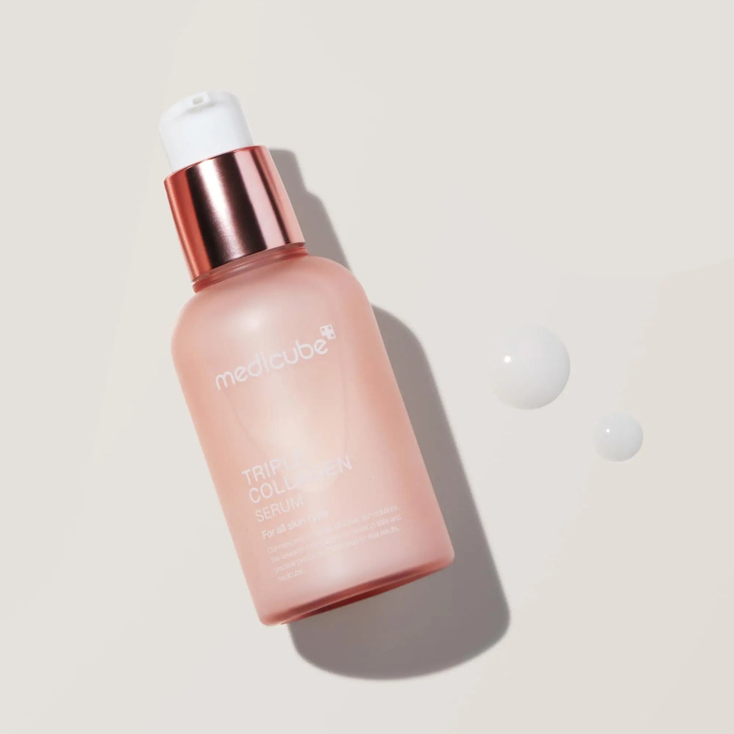 medicube Triple Collagen Serum 55ml bottle with a rose gold pump and two drops of serum on a light background, highlighting facial serum for skin hydration and firmness