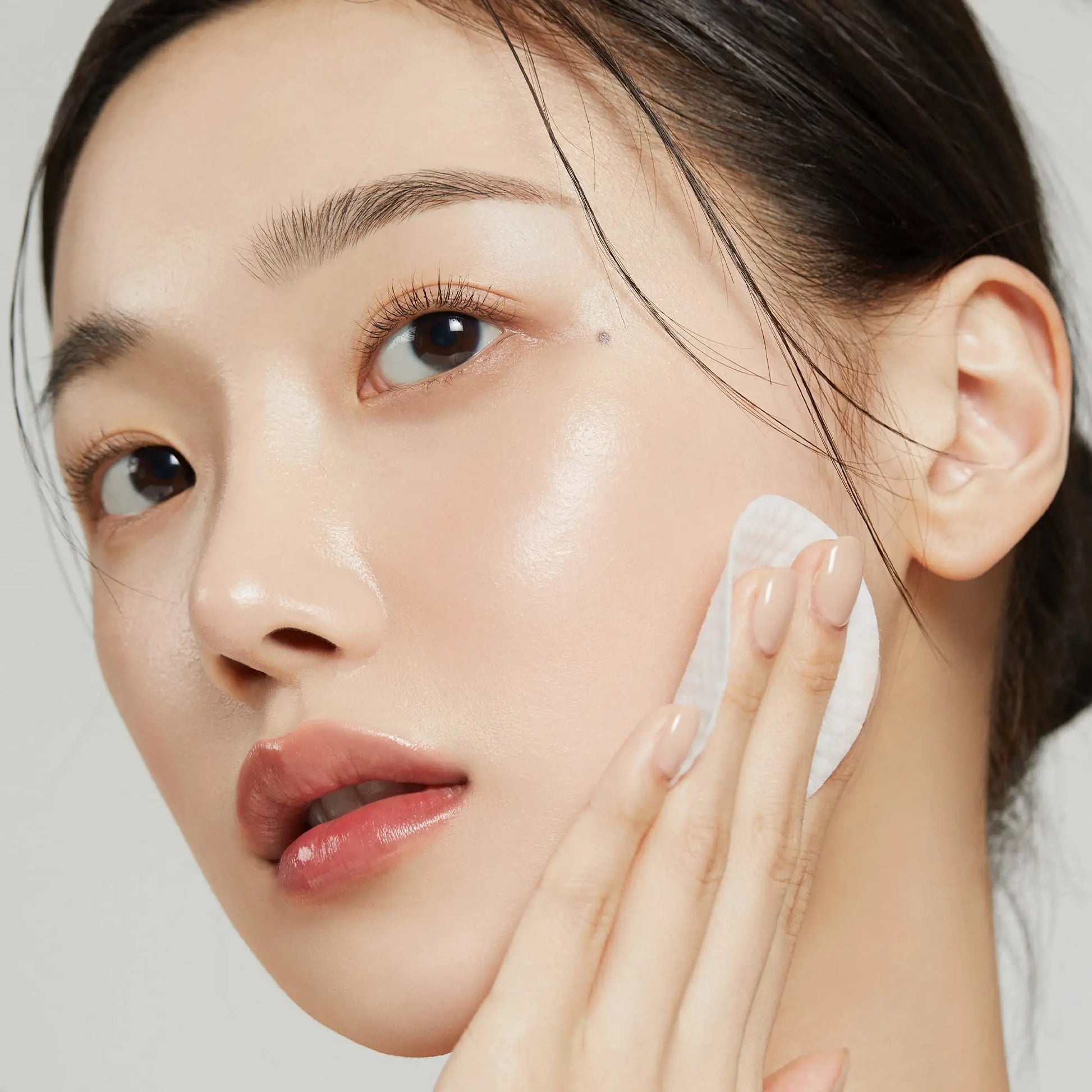 Close-up of a woman gently applying medicube Zero Pore Pads 155g 70pcs to her cheek, showcasing clear, glowing skin and a natural makeup look.