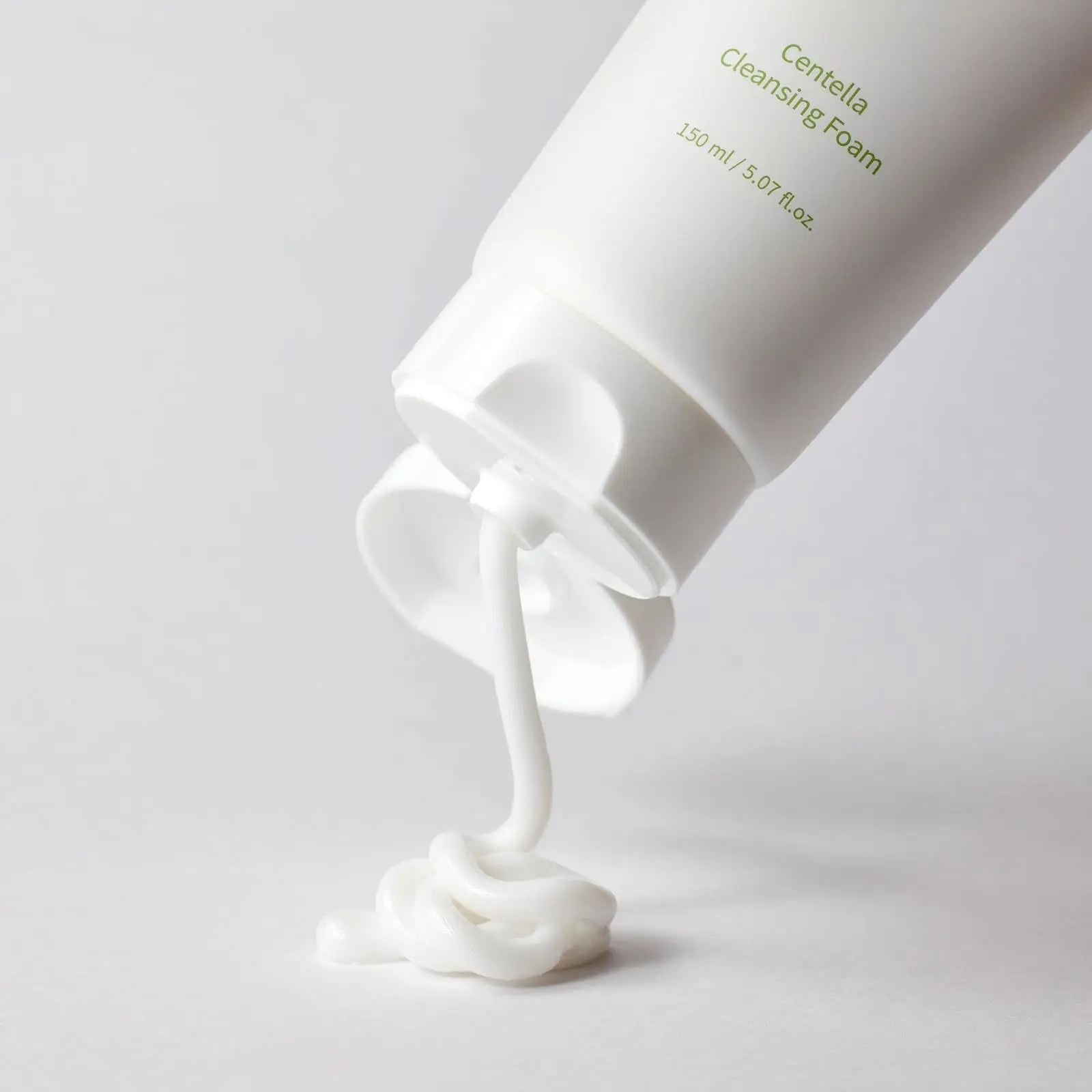White creamy foam being dispensed from a white tube labeled Mixsoon Centella Cleansing Foam 150ml on a light background in a minimalistic style