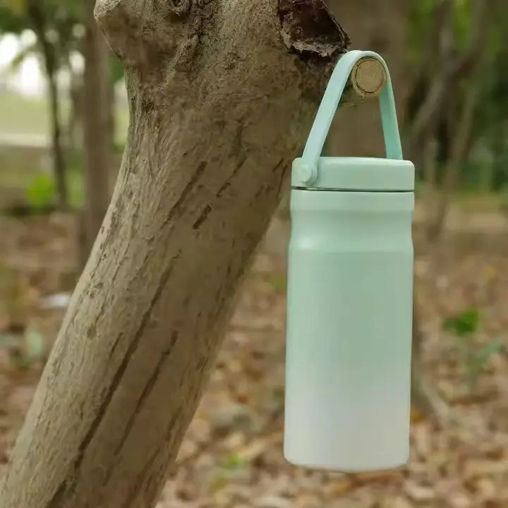Portable Breast Milk and Water Cooler 24-Hour Extended Cooling | Ice-Free Portable Milk Storage for Travel and Work | All-in-One Ice-Free Cooler and Baby Bottle hanging on a tree branch outdoors.