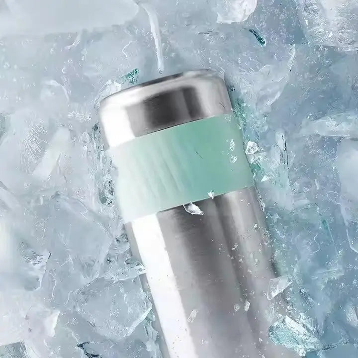 Silver stainless steel cooler surrounded by crushed ice featuring a mint green grip band for the Portable Breast Milk and Water Cooler 24-Hour Extended Cooling | Ice-Free Portable Milk Storage for Travel and Work | All-in-One Ice-Free Cooler and Baby Bottle.