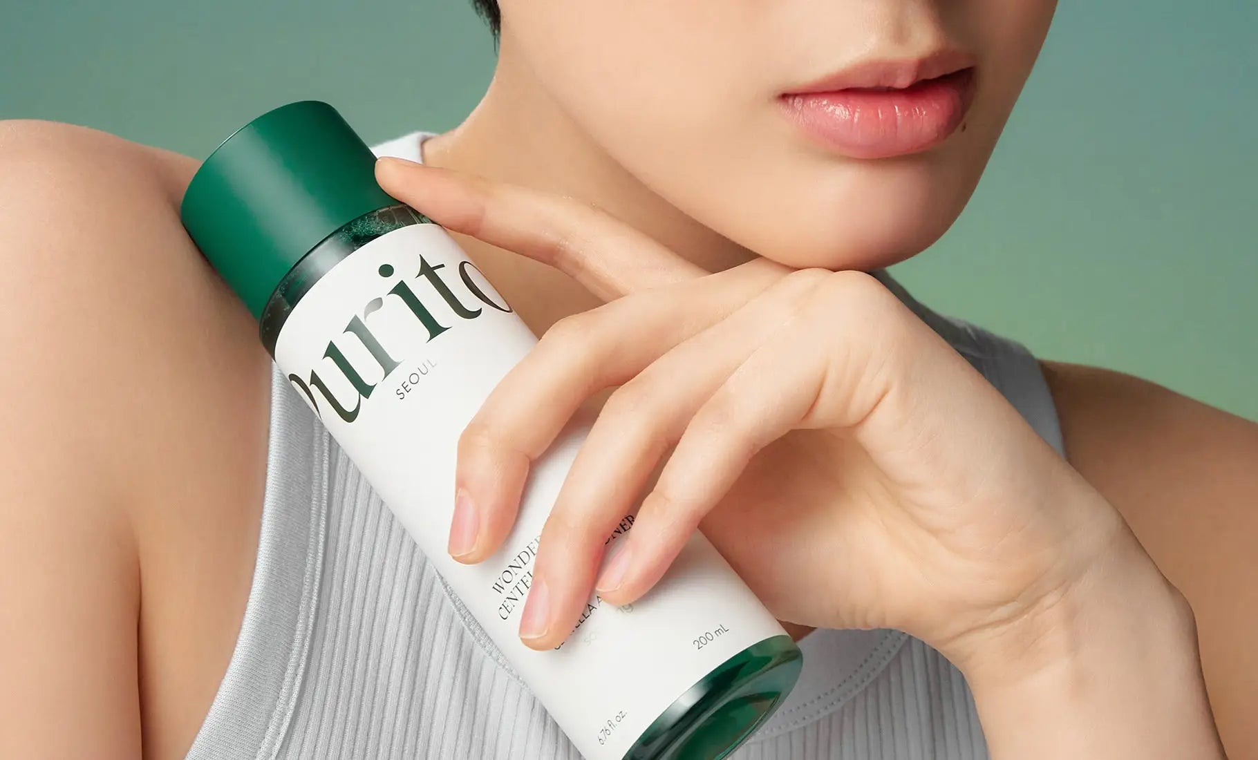 Close-up of a person holding a bottle of PURITO Seoul Wonder Releaf Centella Toner 200ml near their face, showcasing smooth skin and minimalist design.