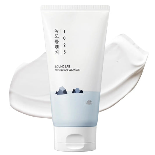Tube of ROUND LAB 1025 Dokdo Cleanser 150ml with Korean text and subtle ocean rock illustration, placed over a smooth white cream texture background.