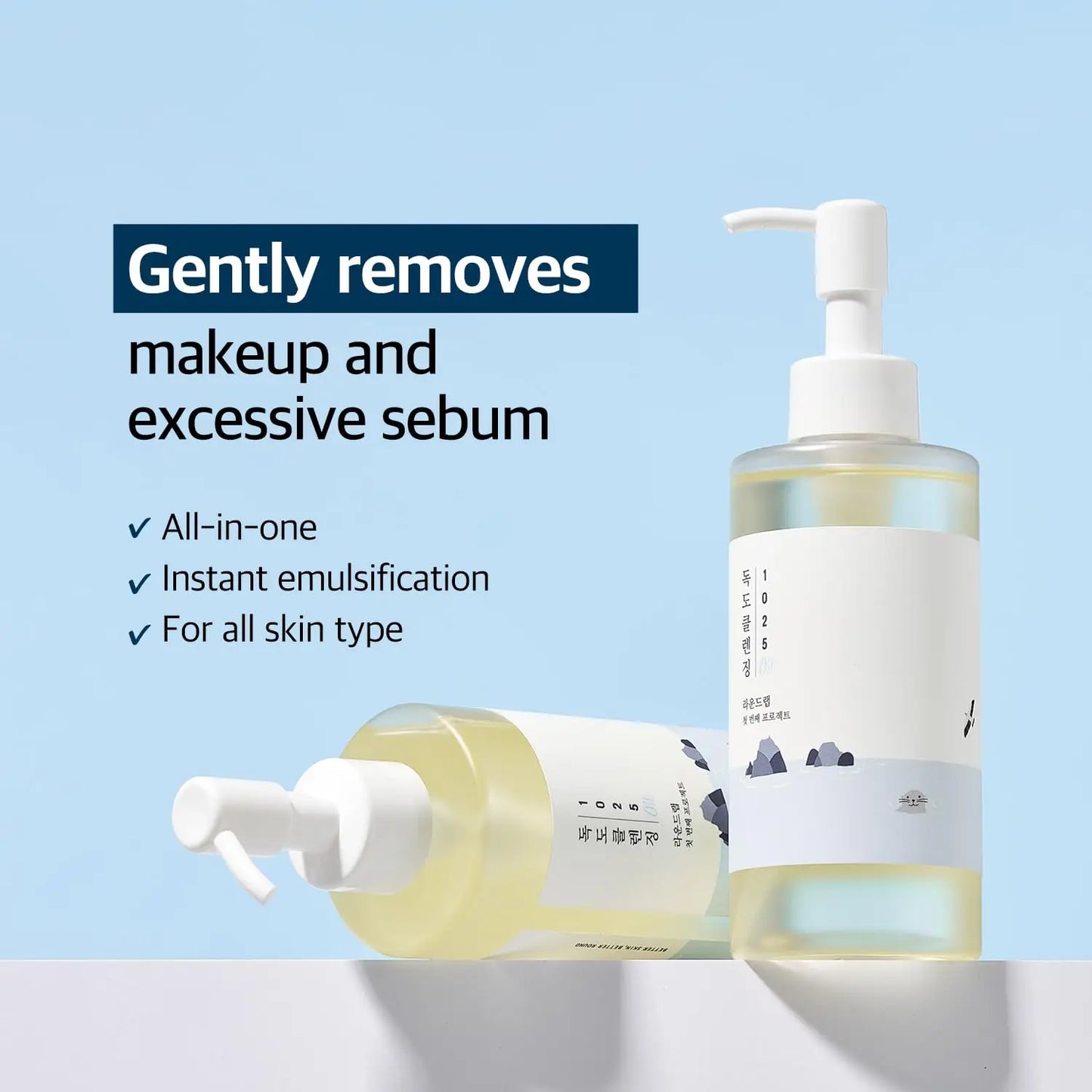Two clear bottles of ROUND LAB 1025 Dokdo Cleansing Oil 200ml with white pumps against a light blue background, highlighting makeup removal and sebaceous control benefits.