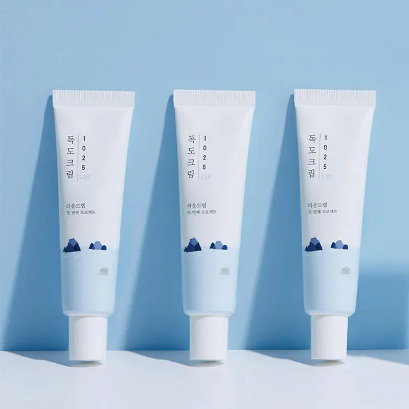 Three tubes of Round Lab 1025 Dokdo Eye cream 30ml with minimalistic white and light blue packaging against a soft blue background