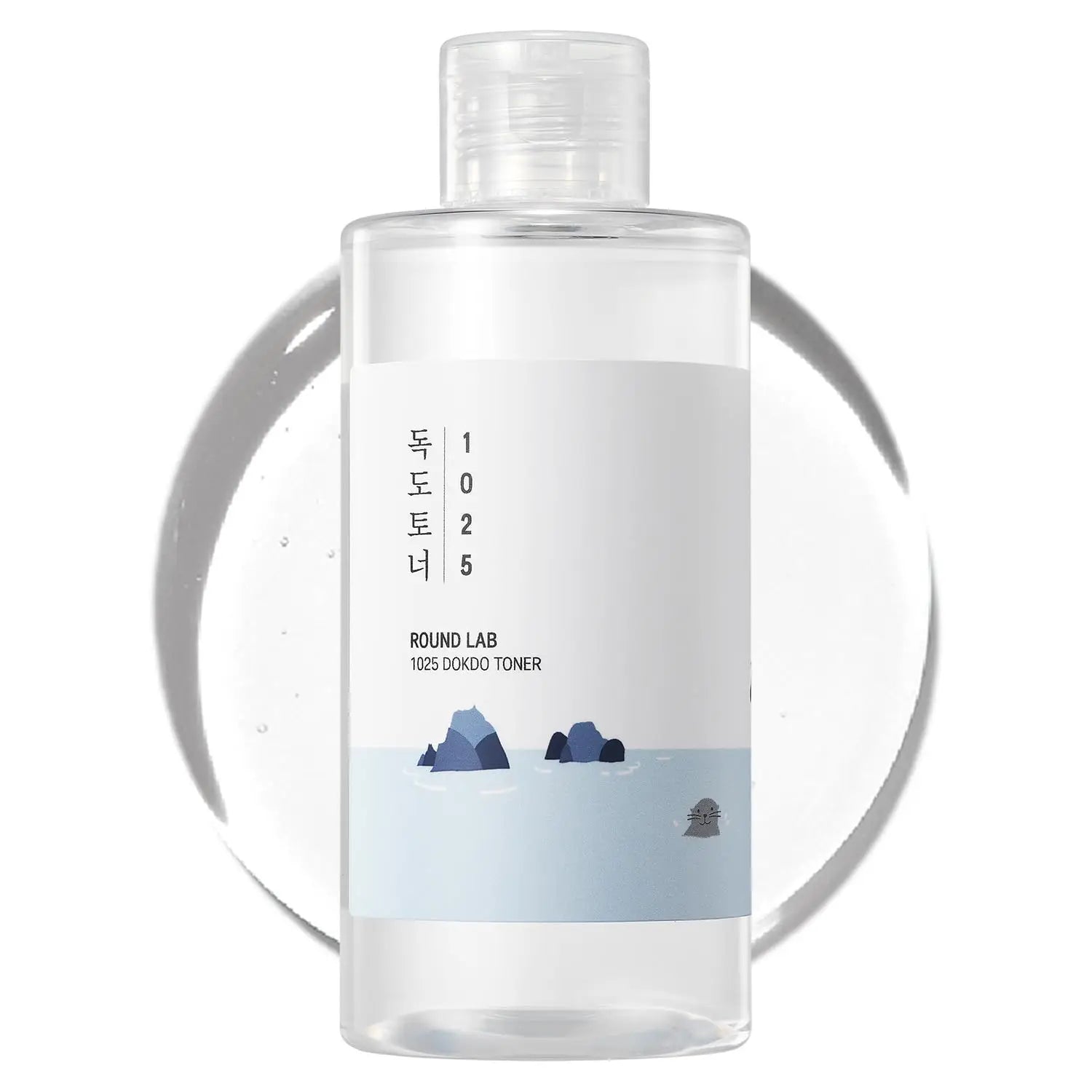 Clear plastic bottle of ROUND LAB 1025 Dokdo Toner 100ml with minimalist white label featuring ocean rocks and gentle waves illustration on a white background with translucent toner drop behind it.