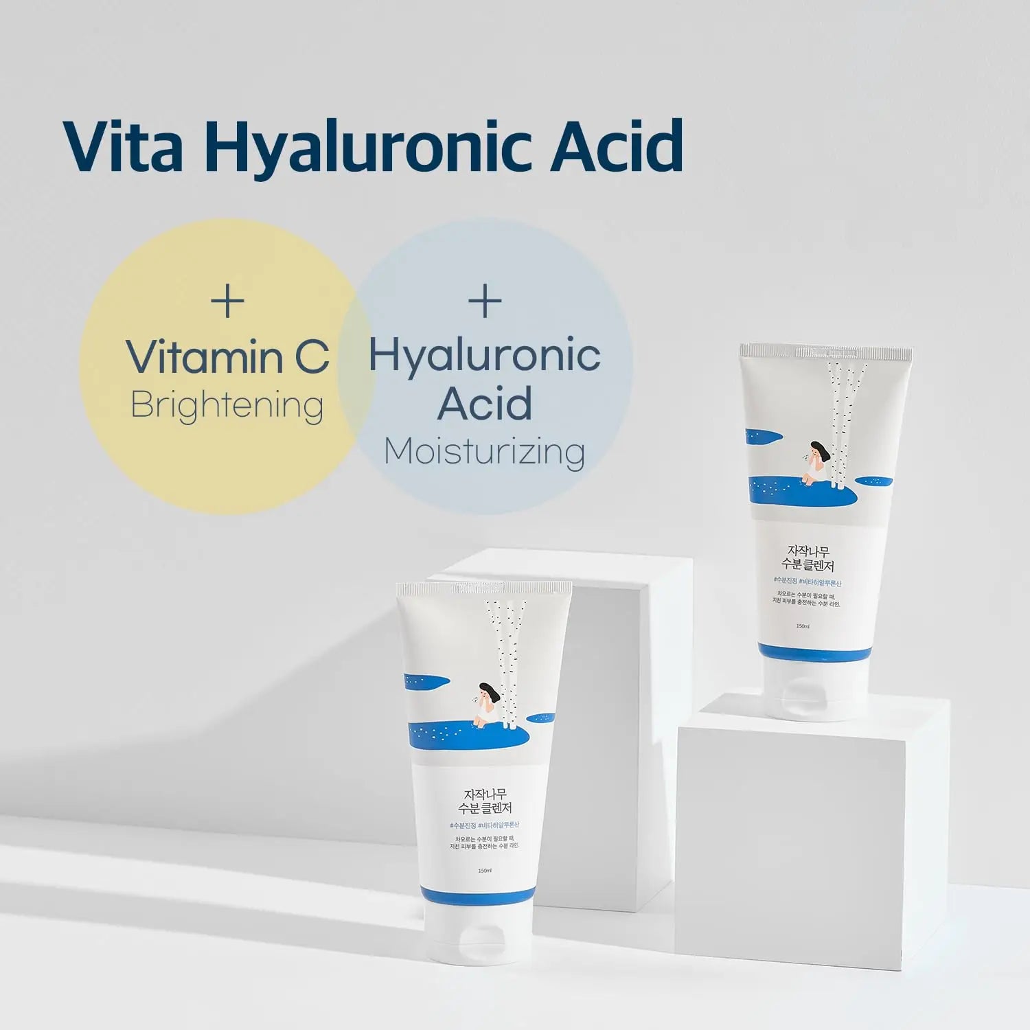 Two tubes of ROUND LAB Birch Juice Moisturizing Cleanser 150ml displayed on white geometric stands with text highlighting Vitamin C brightening and hyaluronic acid moisturizing benefits.