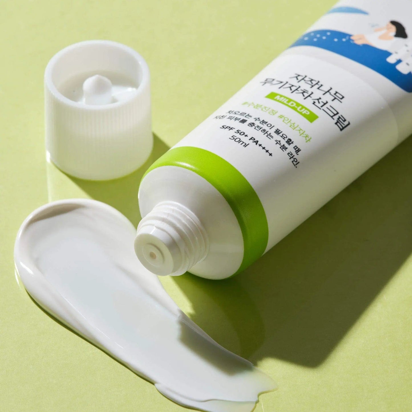 ROUND LAB Birch Juice Moisturizing Mild Up Sunscreen 50ml tube with white cream spilled on a light green surface, showing mild and hydrating sun protection.