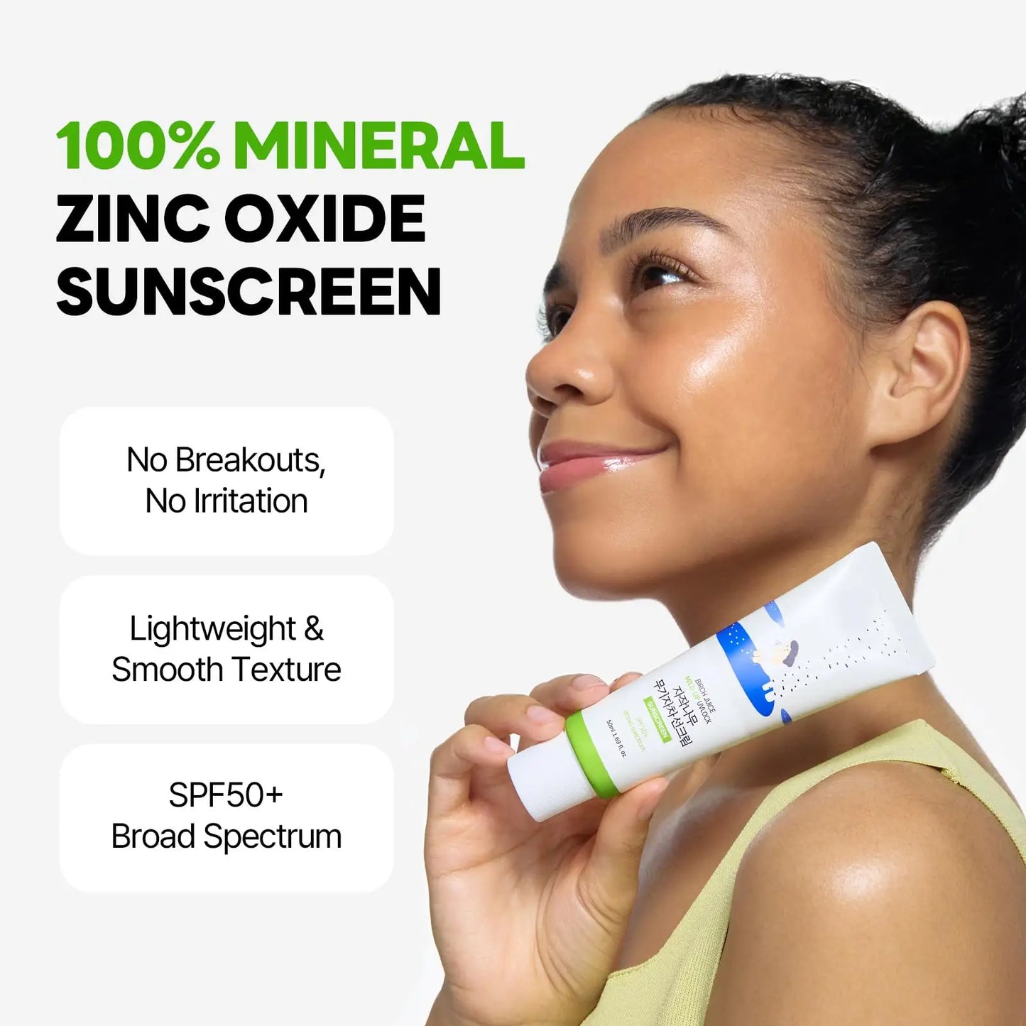 Close-up of a smiling woman with glowing skin holding the ROUND LAB Birch Juice Moisturizing Mild Up Sunscreen 50ml, highlighting its 100% mineral zinc oxide formula with SPF50+ and smooth texture benefits.