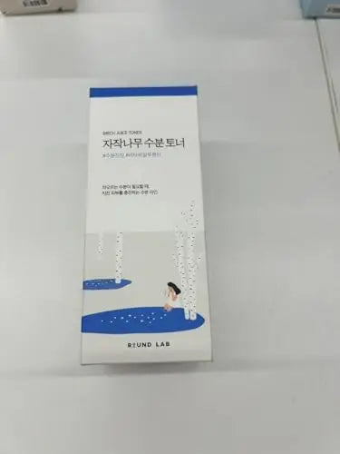 Packaging of ROUND LAB Birch Juice Moisturizing Toner 300ml featuring a simple white and blue design with an illustration of a person sitting among birch trees by a water body.