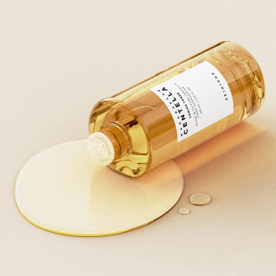 Skin 1004 Madagascar Centella Toning Toner 210 ml bottle lying on its side with clear golden liquid toner spilling onto a light beige surface.